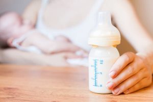Maman qui allaite son bébé au sein avec un biberon de lait dans la main 