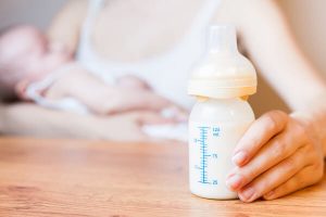 Maman qui allaite son bébé au sein avec un biberon de lait dans la main