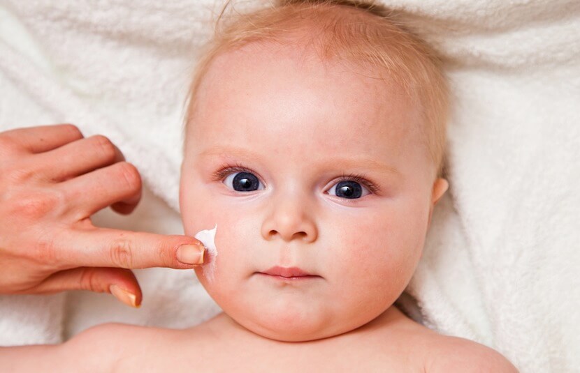 Main passant de la crème sur le visage d'un bébé