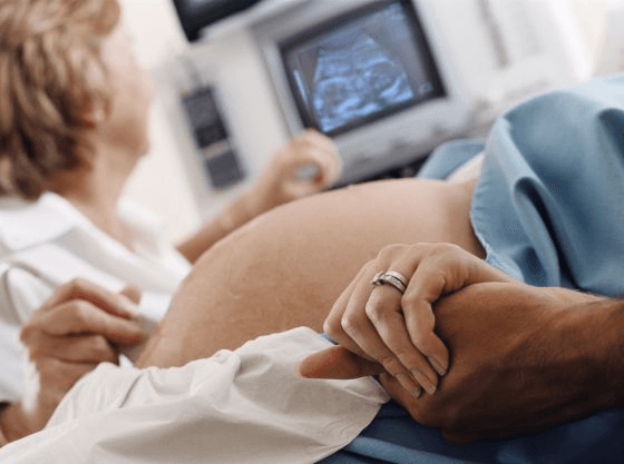 Une femme enceinte qui sert la main de son compagnon à une échographie