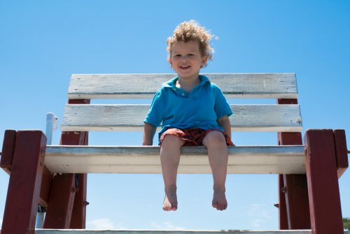 Petit garçon blond assis pieds nus sur un banc