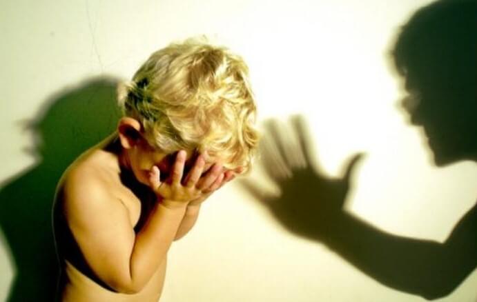 Un enfant se cache la tête dans la main face à un adulte qui le punit,