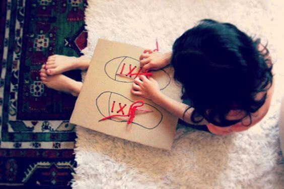 Une petite fille noue et détache les lacets de chaussures sur un jeu en carton
