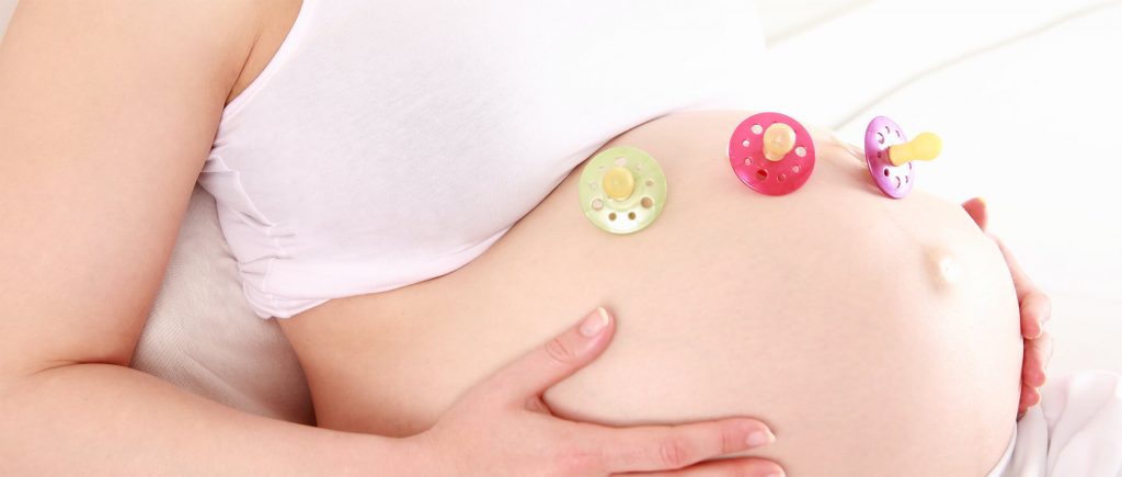 Ventre d'une femme enceinte avec trois tétines posées dessus