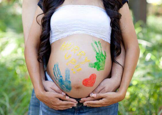 Des dessins à la peinture sur le ventre d'une femme enceinte, dans les bras de son compagnon