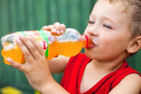 Un petit garçon en train de boire une boisson chimique, un aliment dangereux pour la santé à éviter