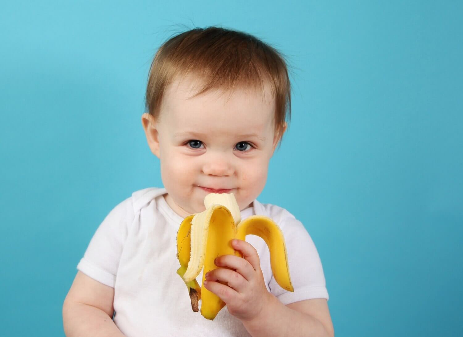 Un bébé mange une banane qui fait partie de l'alimentation complémentaire