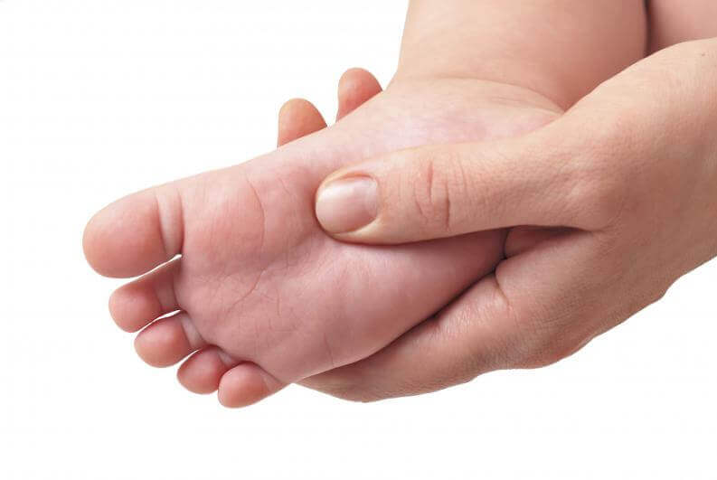 Le pied nu d'un bébé dans la main d'un adulte, une étape importante avant de choisir des chaussures pour enfants