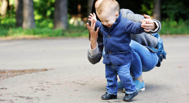 Un bébé marche avec l'aide de sa maman dans un parc