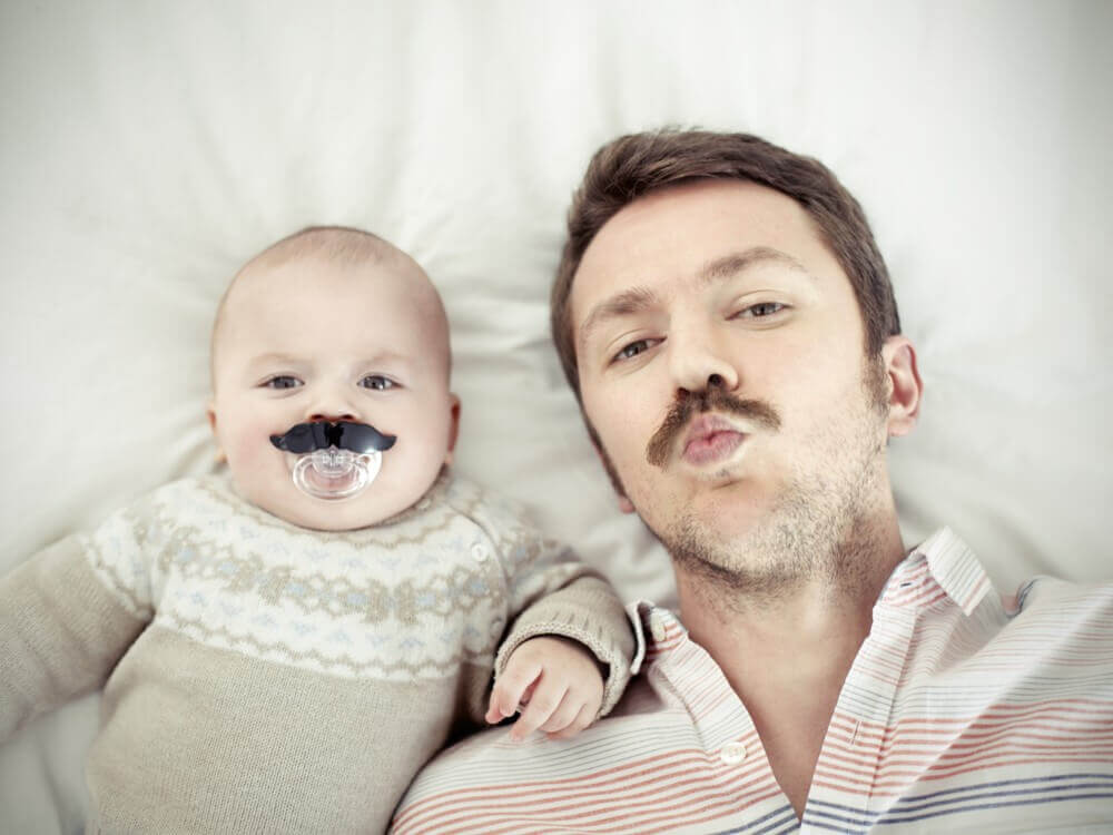 Un papa qui pose à côté de son bébé avec une fausse moustache