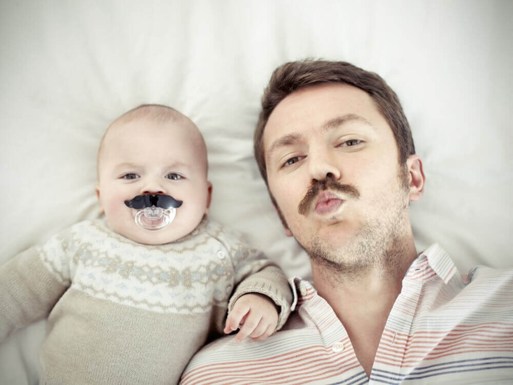 Un papa qui pose à côté de son bébé avec une fausse moustache 