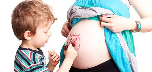 Un enfant dessine sur le ventre de sa mère qui attend un deuxième enfant