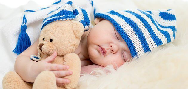 Bébé endormi avec une peluche et un bonnet sur la tête 