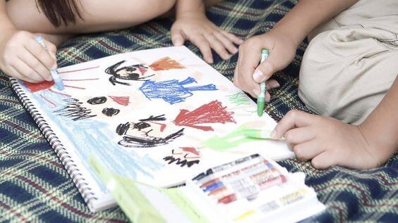 Deux enfants dessinent au crayon sur un cahier, activité qui peut stimuler la psychomotricité fine