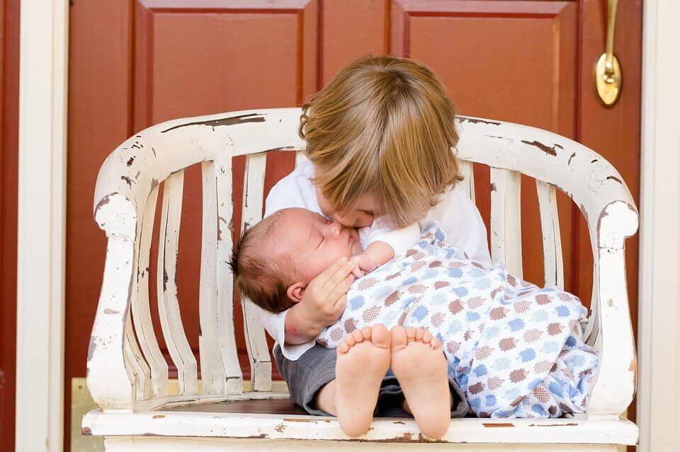 Un petit garçon avec sa petite sœur bébé dans les bras 