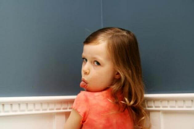 Une petite fille au coin tire la langue, un signe d'impolitesse qui peut être dû à des parents trop permissifs