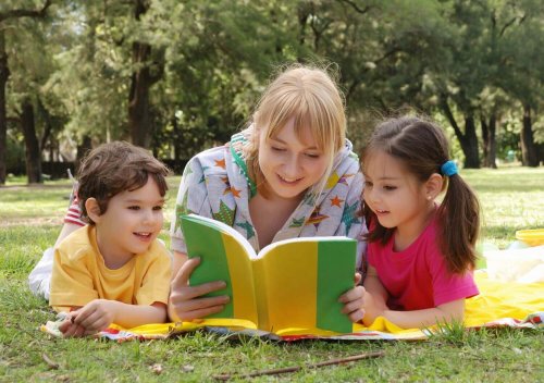 Une mère lit dans un parc un livre pour enfants à un petit garçon et une petite fille