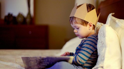 Un petit garçon en pleine lecture avec une couronne sur la tête