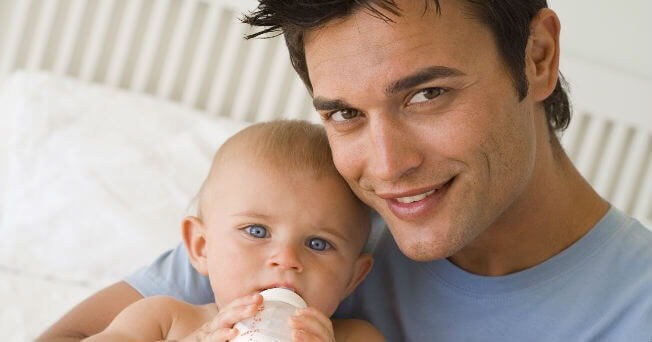 Un papa tient son bébé avec son biberon dans ses bras