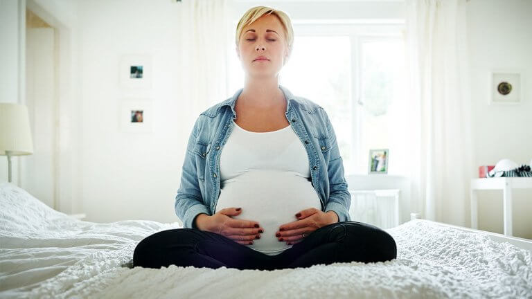Femme enceinte en séance de méditation sur son lit, avant l'arrivée du bébé