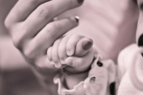 Un bébé tient le doigt de sa maman dans sa main