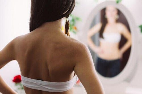Une adolescente observe son corps dans un miroir.
