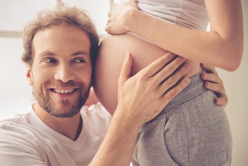 Un homme écoute son bébé au travers du ventre de sa femme