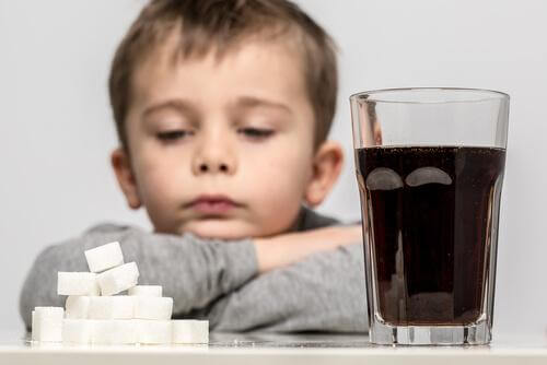 Un enfant devant un verre de soda et son équivalent en sucre