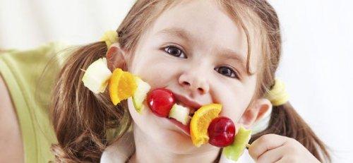 Une fille mange une brochette de fruits
