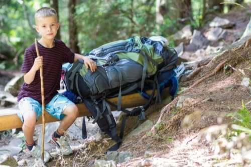 Enfant qui pose à côté d'un gros sac à dos de randonnée en forêt 