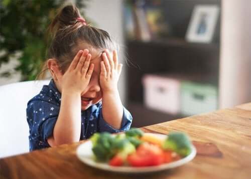 Une enfant qui se cache les yeux devant des légumes