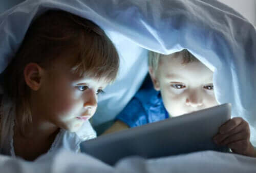 deux enfants regardant un film sur une tablette sous la couverture