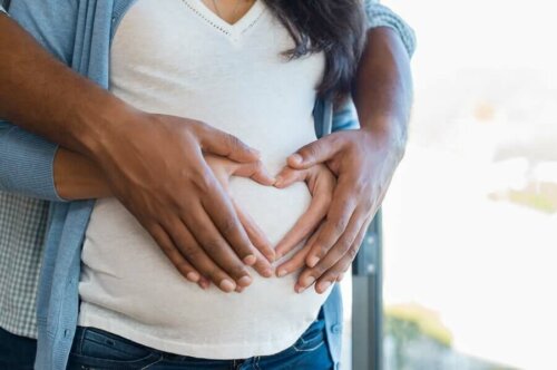 Une femme enceinte avec son partenaire qui forment un coeur sur le ventre avec leurs mains. 