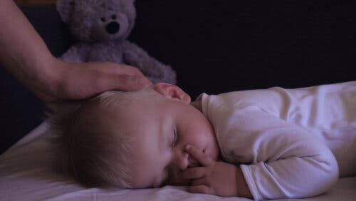 Un bébé en train de dormir avec sa mère qui le caresse.