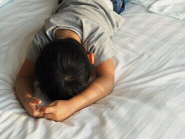 Un enfant allongé sur un lit qui se cache la tête.