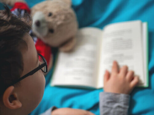 Un enfant en train de lire un livre avec des lunettes et sa peluche.