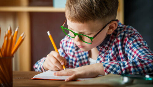 Un enfant apprend à écrire avec des lunettes et une chemise.