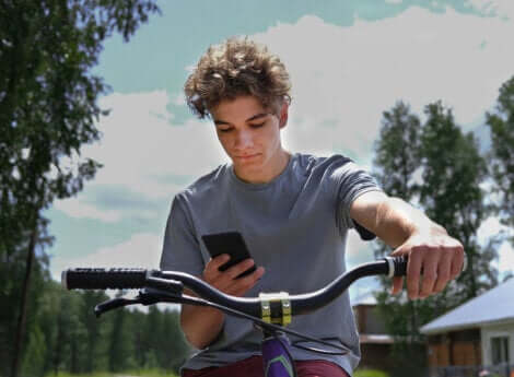 Un adolescent qui roule à vélo avec son portable.
