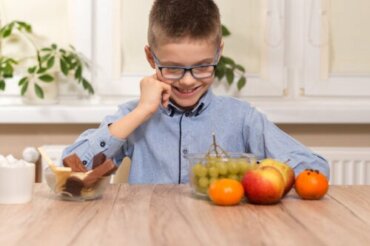 Un jeune garçon qui doit choisir entre des fruits et du chocolat.