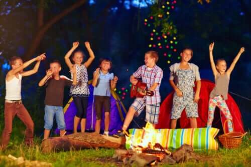 des enfants heureux chantent et dansent au camp d'été du feu de joie