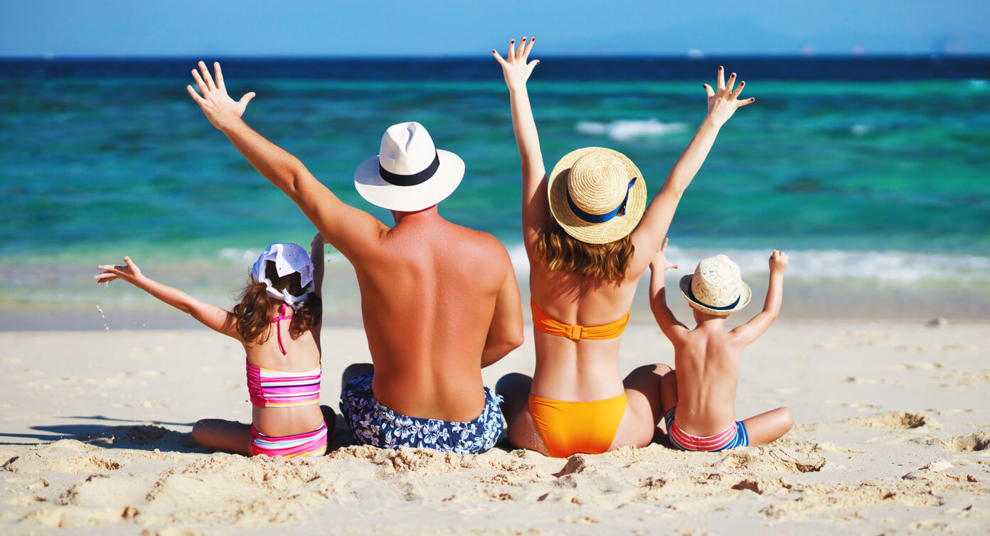 famille de dos sur la plage levant les bras