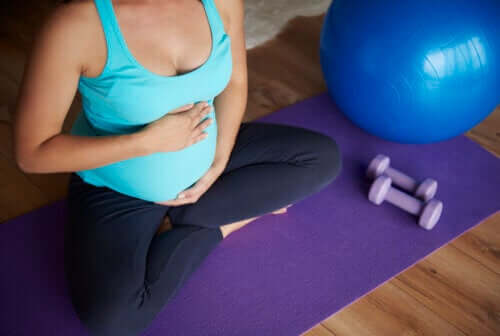 femme enceinte assise sur le sol sur un tapis de yoga avec des haltères et une balle de fitball pilates