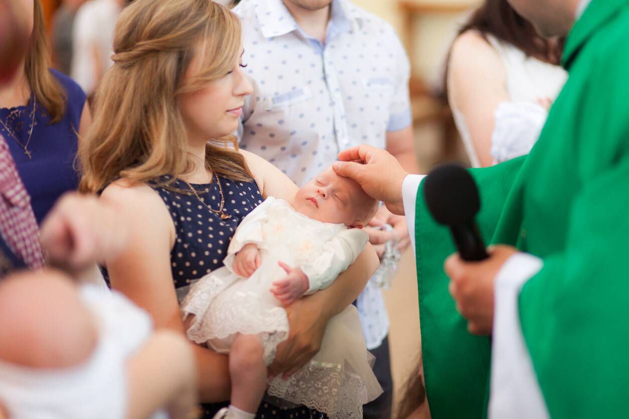 Une maman qui tient son bébé dans ses bras lors de son baptême.